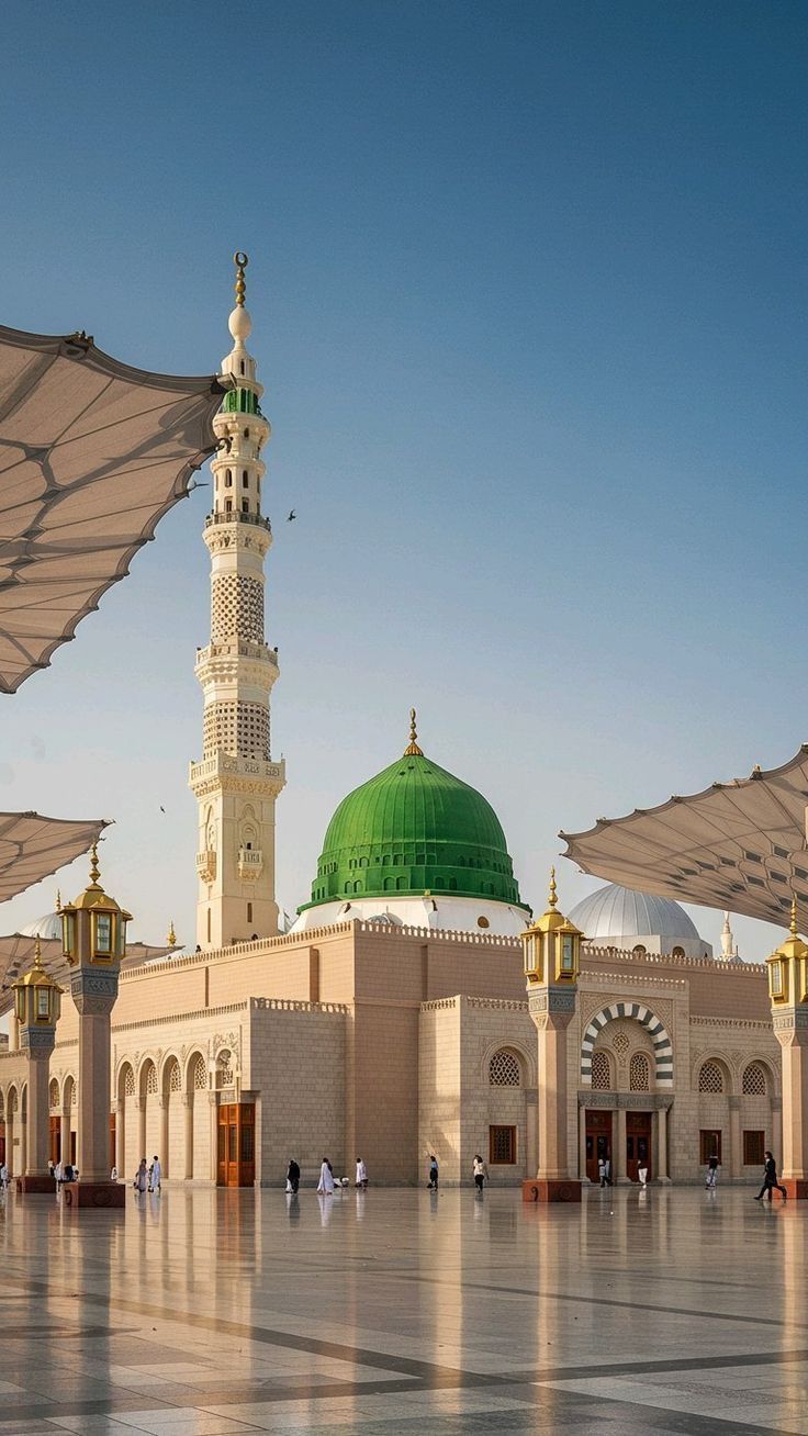 La mosquée du Prophète à Madinah : minaret, coupole verte et grandes ombrelles ouvertes sous un ciel bleu.