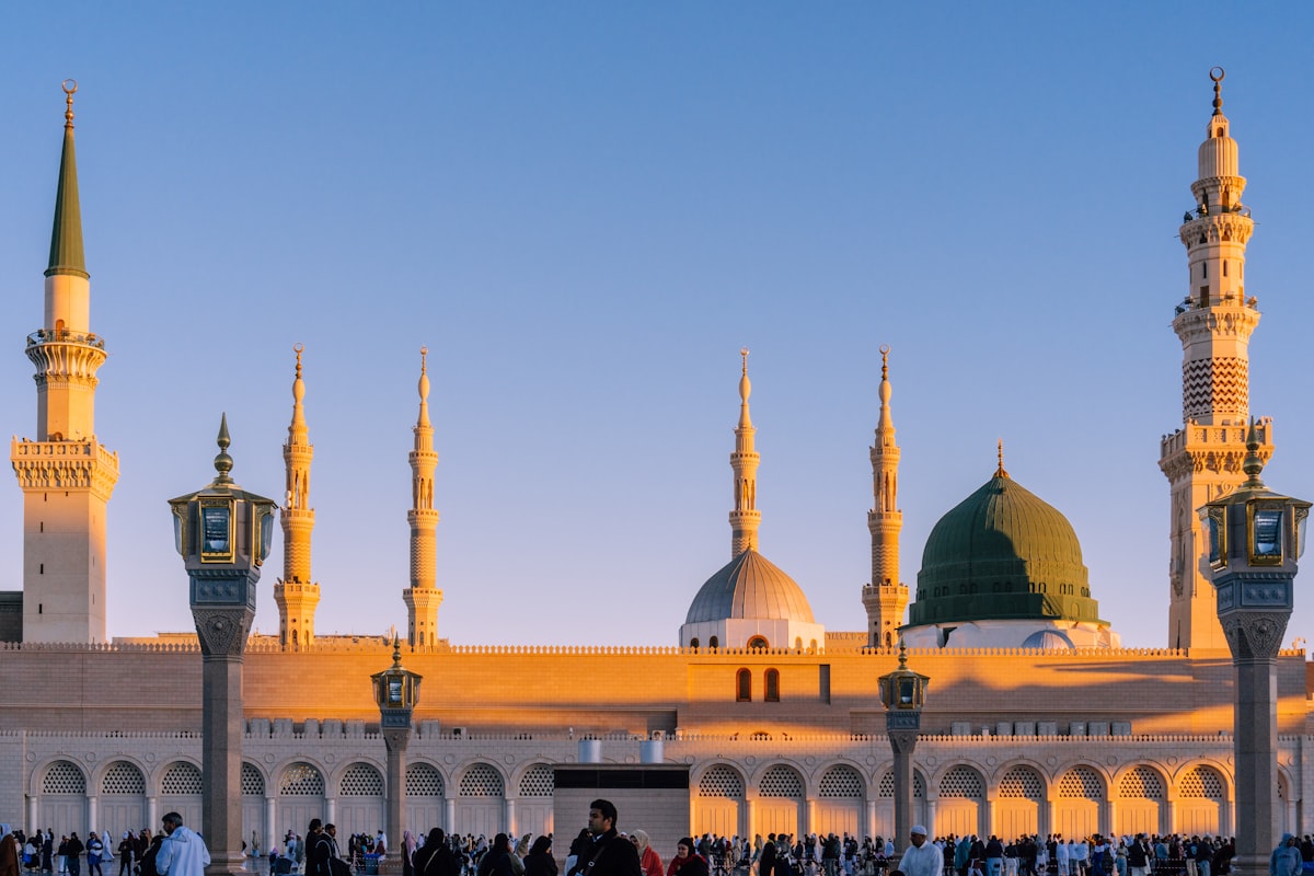 La mosquée du Prophète à Madinah à l’heure dorée, minarets illuminés et coupole verte.