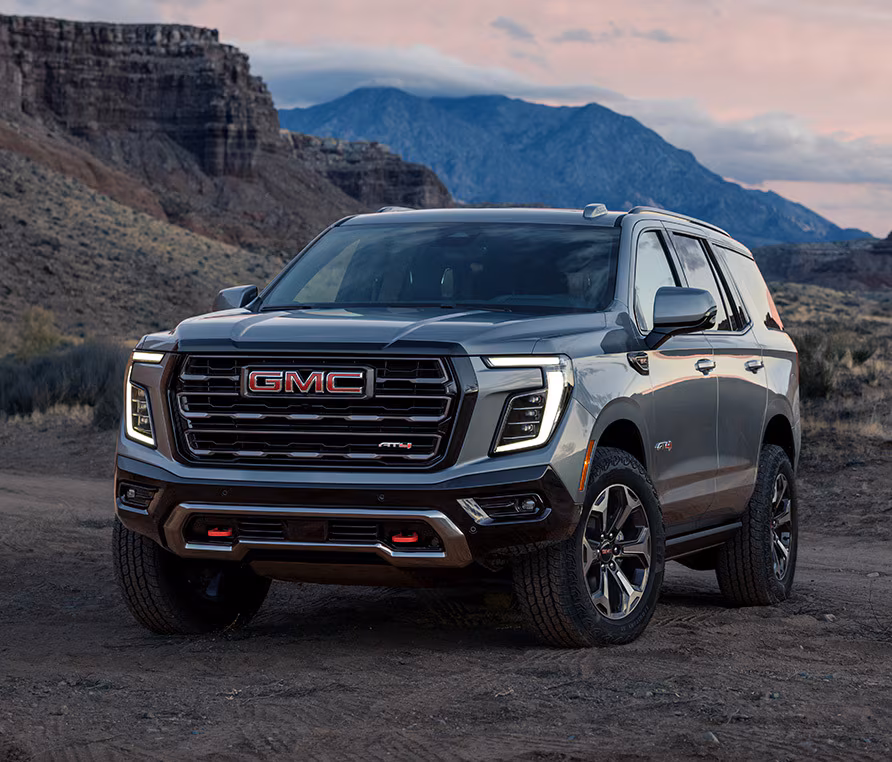 SUV GMC gris foncé garé au pied de reliefs rocheux, sous un ciel de fin de journée.