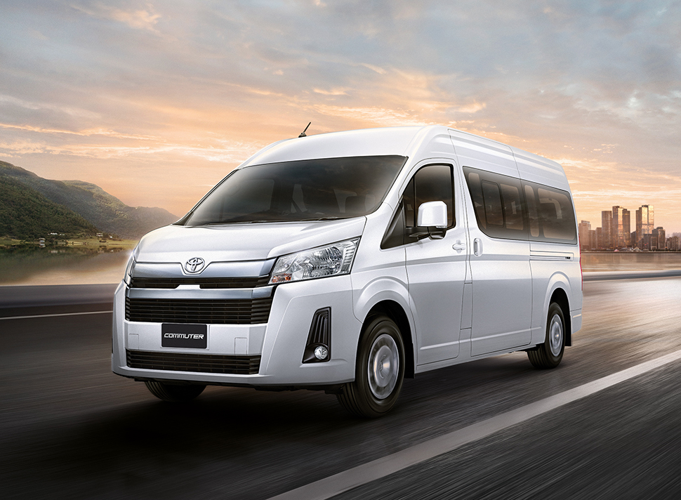 Minibus Toyota Hiace blanc roulant sur une route au coucher du soleil.