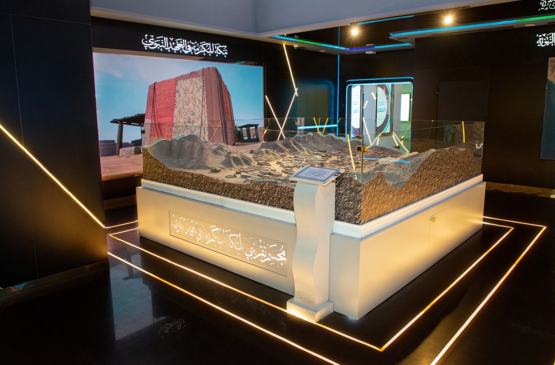 Maquette exposée dans un musée, soulignée de filets lumineux, sous une inscription calligraphiée.
